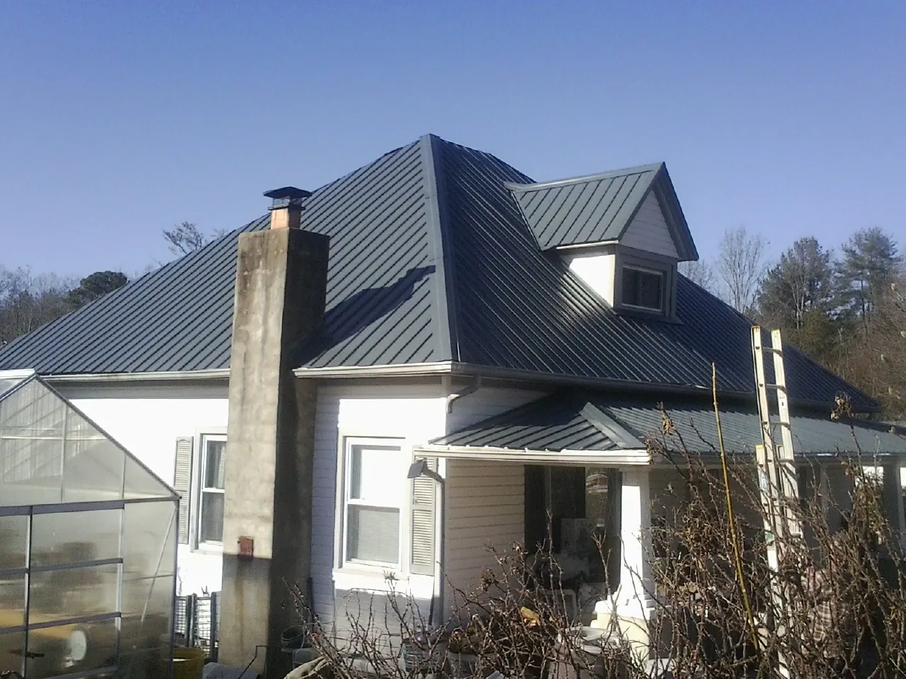 Dark blue standing seam metal roof on a white farmhouse with dormer — Slate & Tile Roof Repair by Roofing Brothers in Beaver Creek