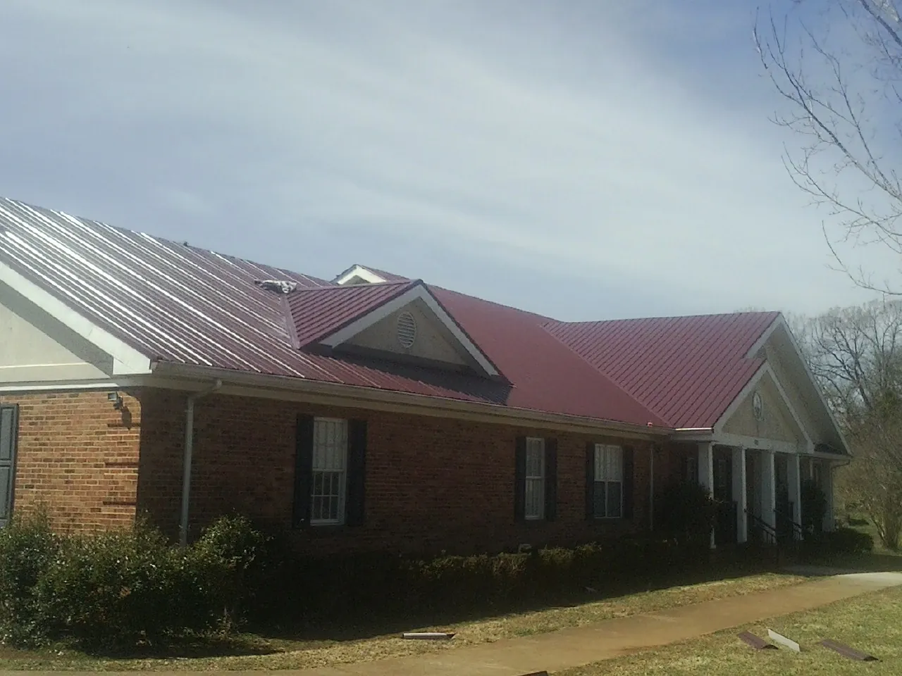 Red metal roof with gabled entries on a long brick building, from a Hail Damage Roof Repair job in Beaver Creek
