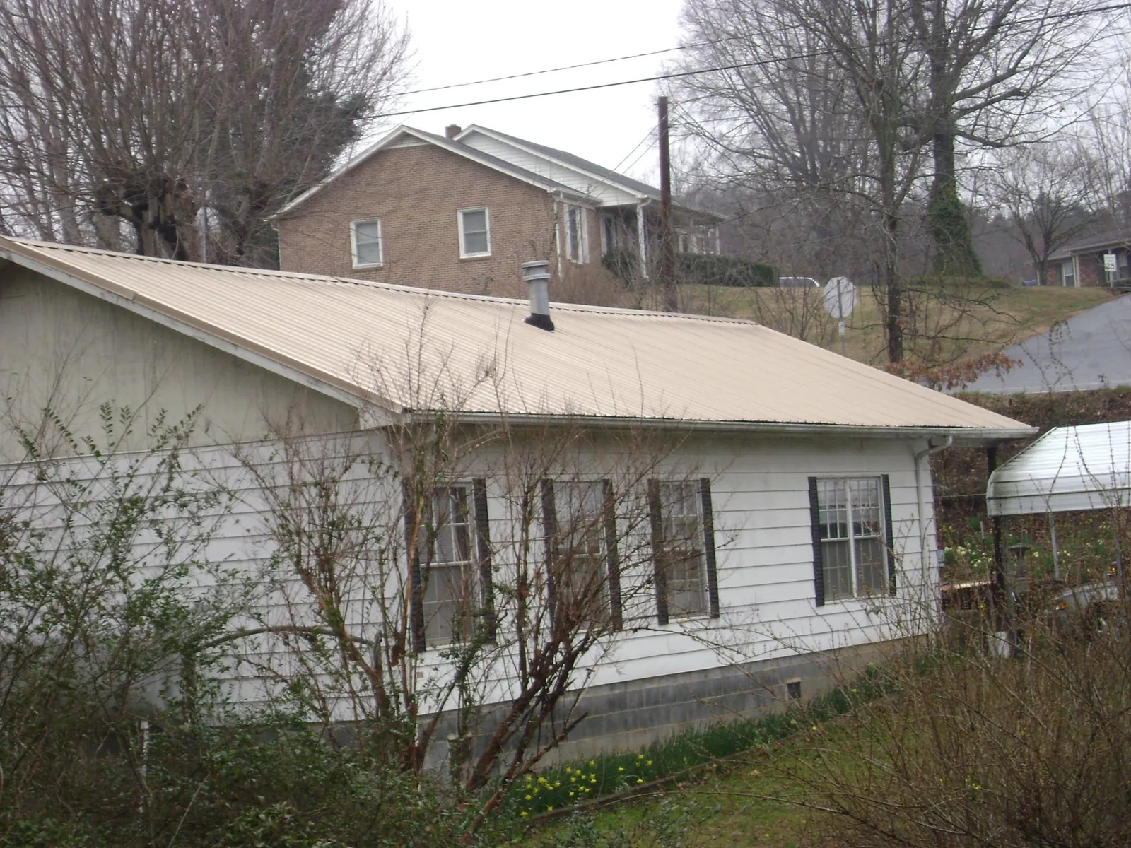 Tan metal roof on a white sided house set into a hillside — Commercial Roofing by Roofing Brothers in Beaver Creek