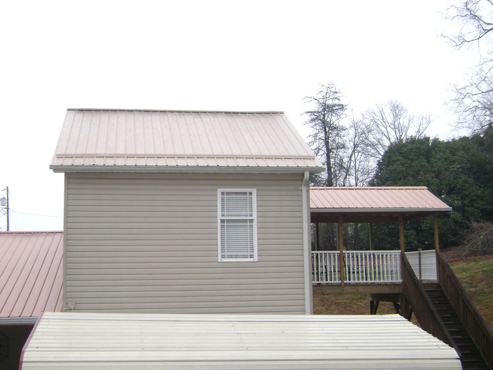 Tan metal roofs on a two story addition and attached porch, from a Roof Replacement job in Beaver Creek